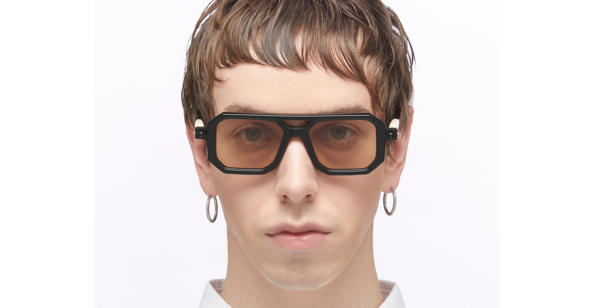 Person with short brown hair wears KUBORAUM P8 large black rectangular eyeglasses and hoop earrings, shown from the front.