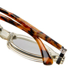 Close-up of Kuboraum Q7 eyeglasses with clear frames and tortoiseshell-patterned temples, highlighting the hinge and part of the lens against a white background.