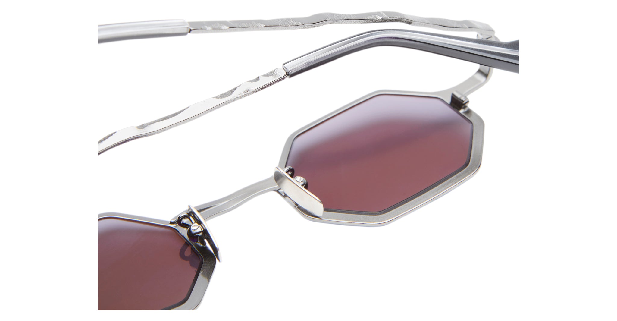 Close-up of Kuboraum Z19 sunglasses with octagonal, burgundy-tinted lenses and thin silver metal frames featuring a wavy, textured temple design.