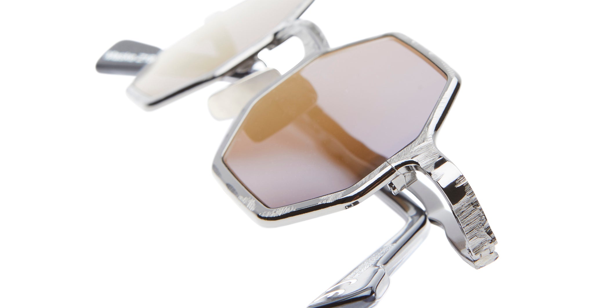 Close-up of Kuboraum Z19 geometric sunglasses featuring brown-tinted lenses and sleek silver frames, shown partly folded against a white background.
