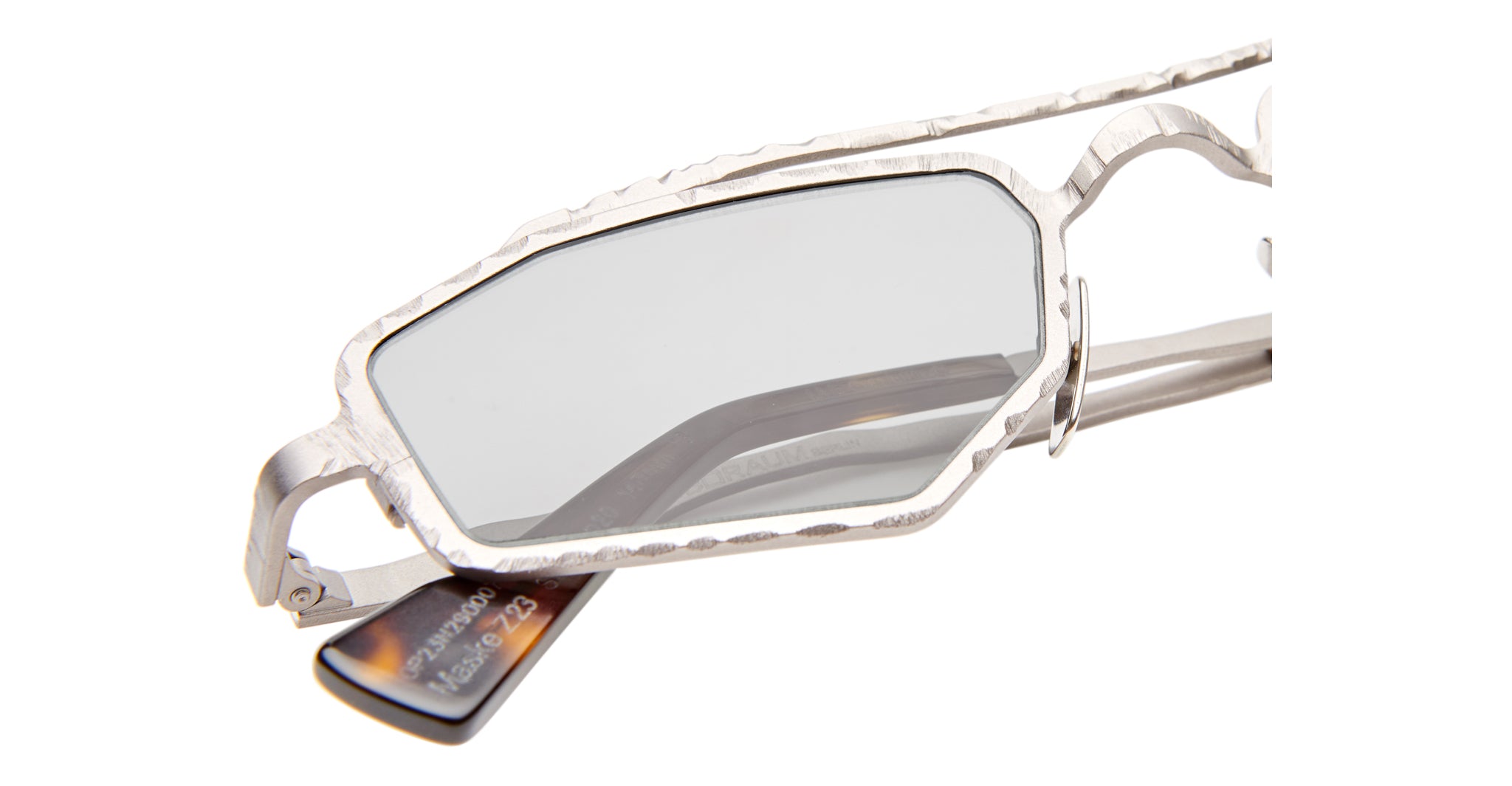 Close-up of Kuboraum Z23 sunglasses featuring an irregular, angular silver metal frame and gray-tinted lenses. A visible tag is attached to one arm, set against a white background.