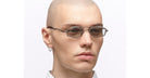 A person with a shaved head wears Kuboraum Z23 geometric sunglasses and a hoop earring, staring straight ahead against a plain white background.