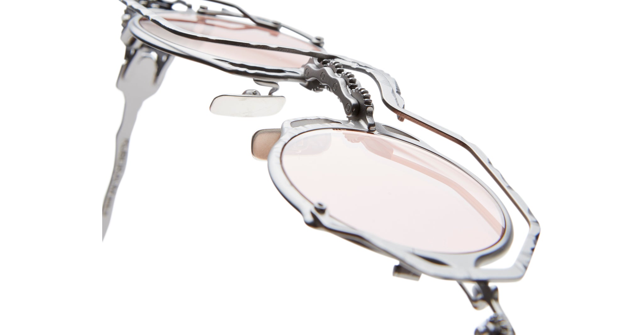 Close-up view of the Kuboraum Z50 sunglasses, featuring light pink lenses and an intricate metallic sculptural frame, set against a white background.