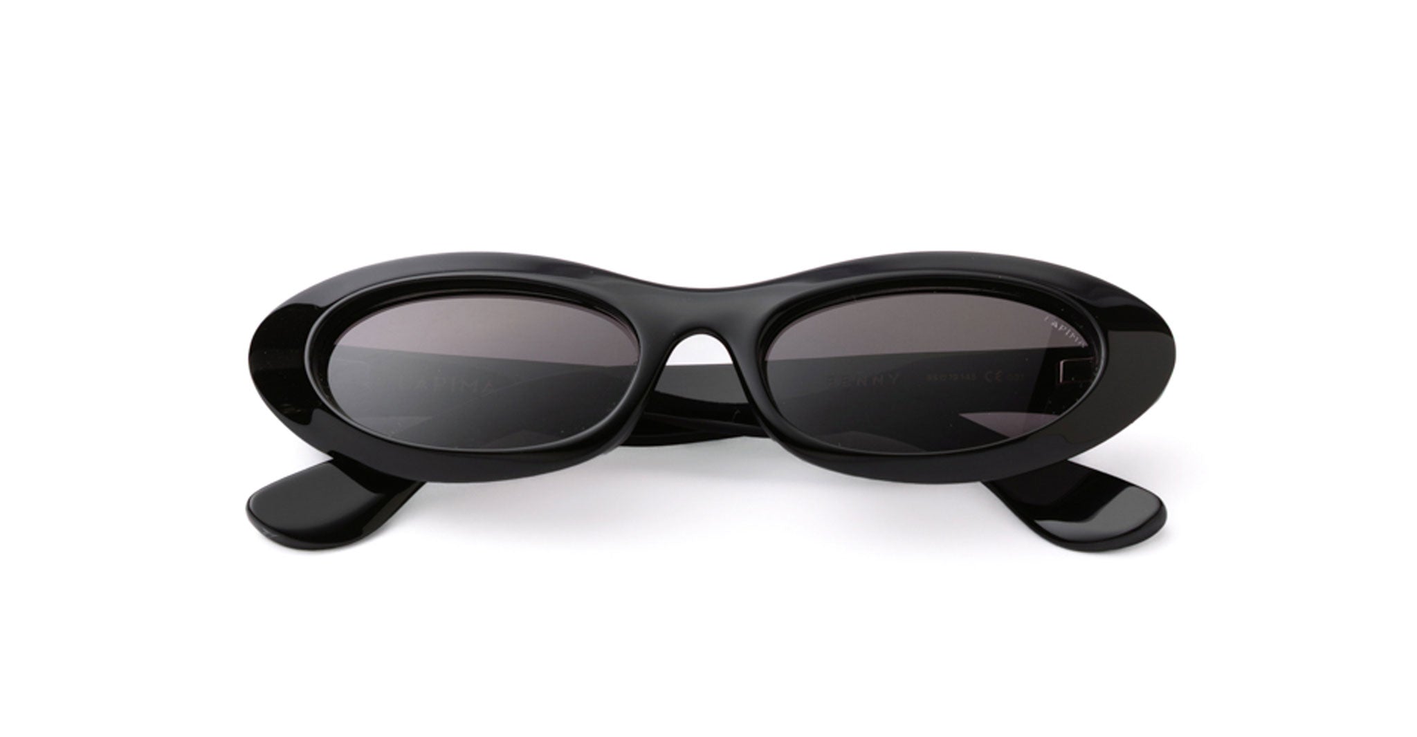 Front view of Lapima Penny sunglasses in Black Shadow, featuring a glossy black acetate frame with narrow oval lenses, bold elongated outer edges, a sculpted bridge with a distinctive cutout, dark gray tinted lenses, and wide matching acetate temples.