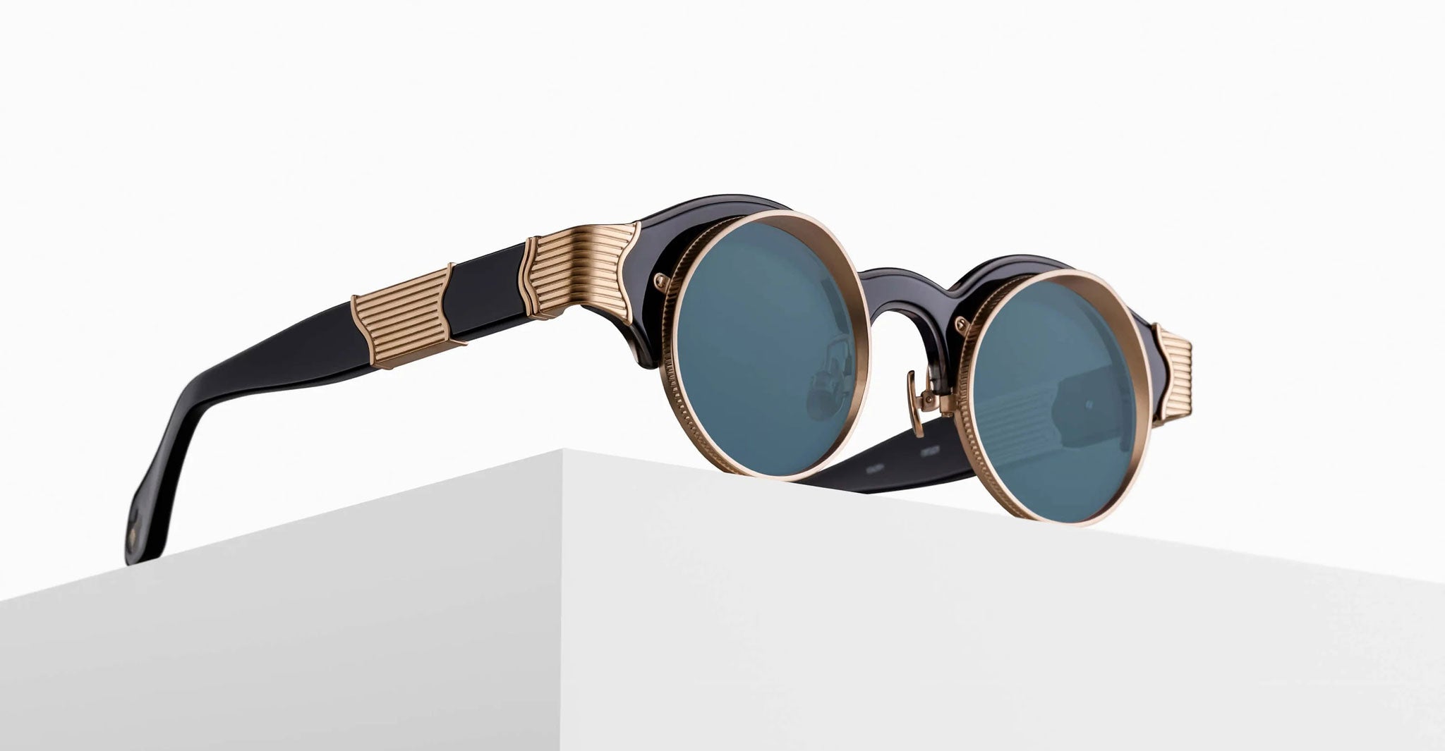 The Matsuda 10605H round sunglasses feature blue lenses, black frames, and gold accents, displayed on the edge of a white surface against a plain white background.