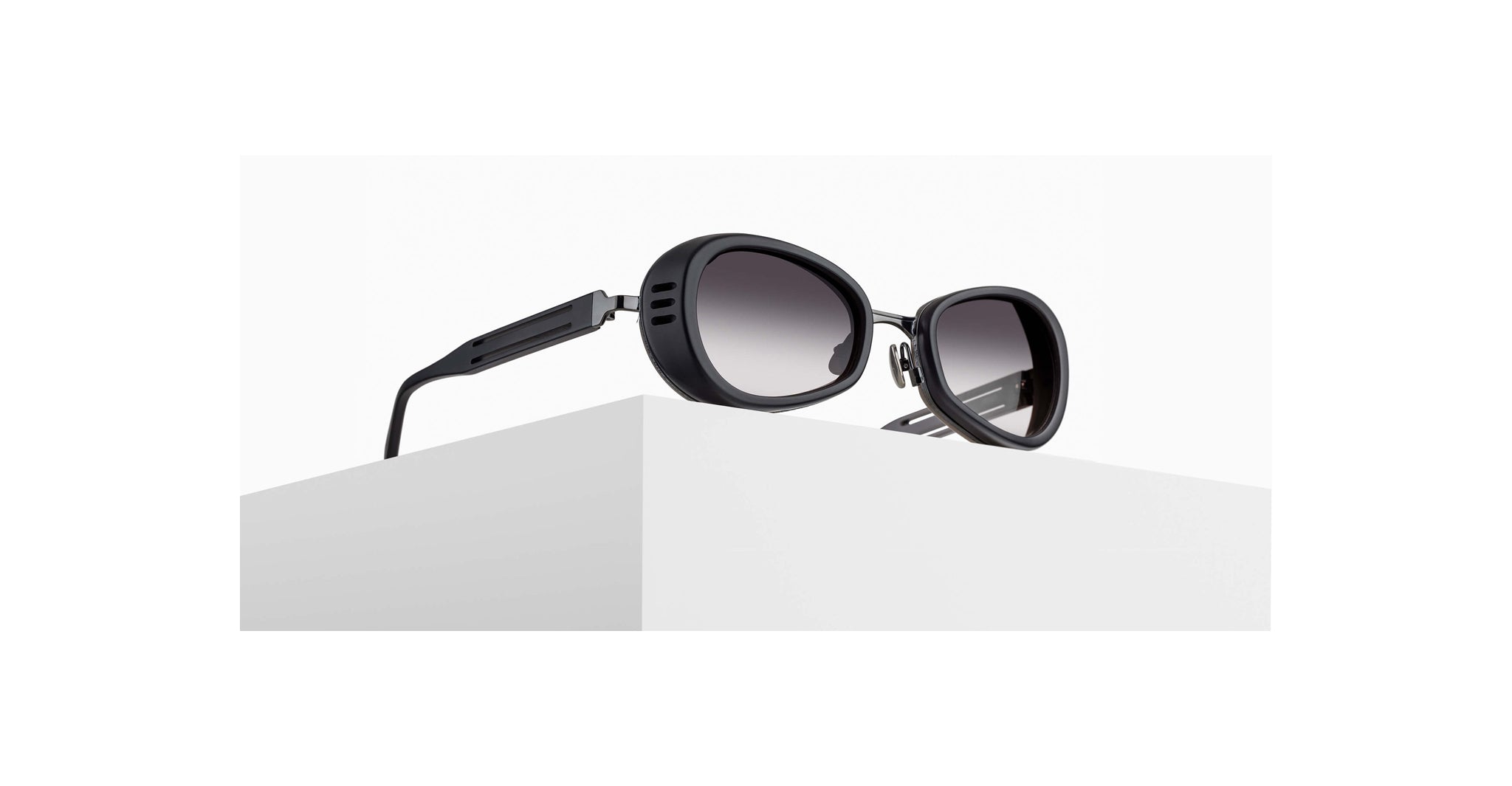 3/4 view of Matsuda 10616H sunglass in matte black with grey gradient lenses on a pedestal