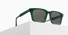 A pair of Matsuda M1040 sunglasses with green frames and dark lenses rests on the edge of a white, geometric surface against a plain light background.