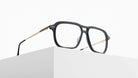 The Matsuda M2062 rectangular black eyeglasses with thin gold arms are showcased on a minimalist white surface against a plain white background.