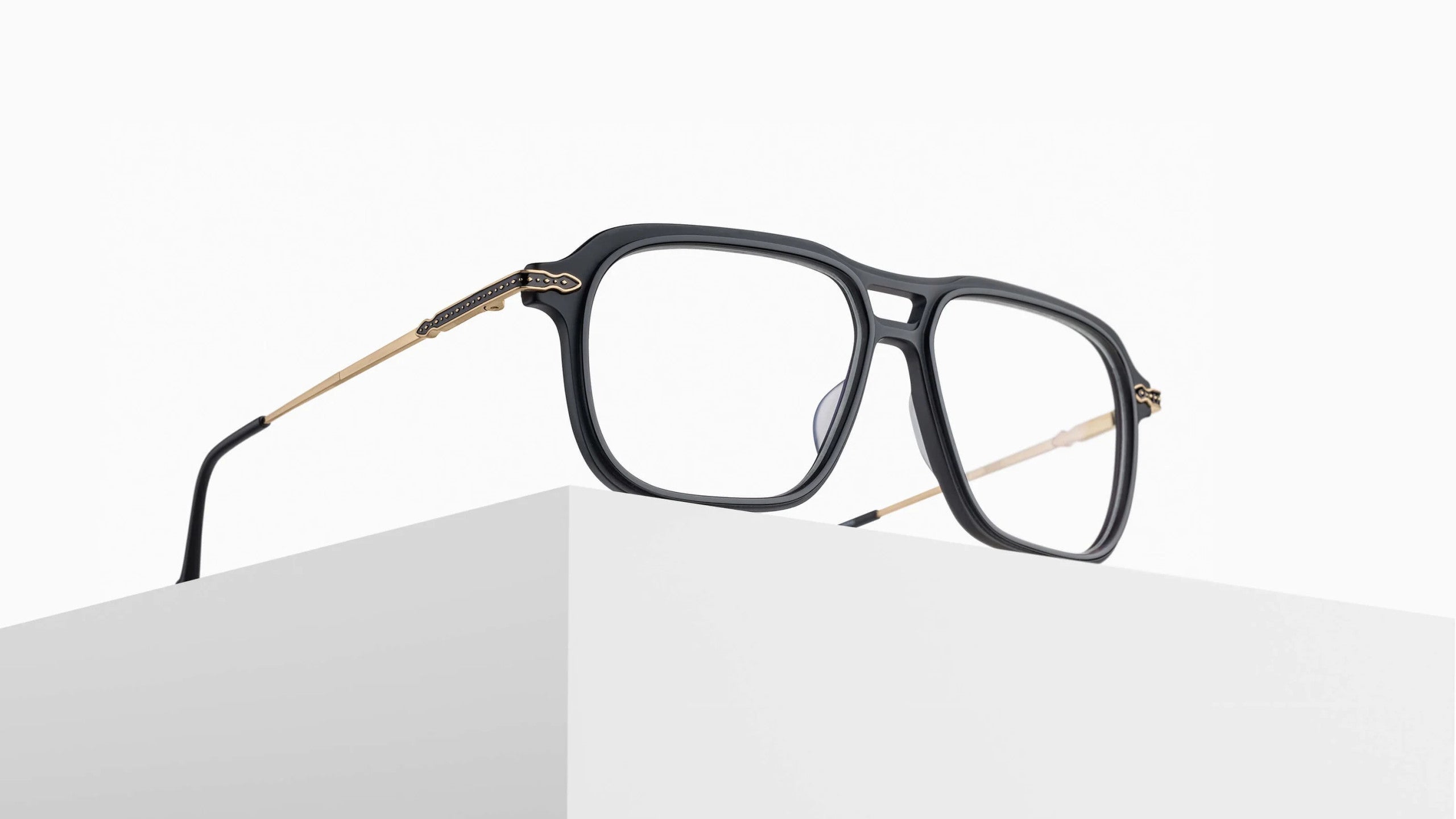 The Matsuda M2062 rectangular black eyeglasses with thin gold arms are showcased on a minimalist white surface against a plain white background.