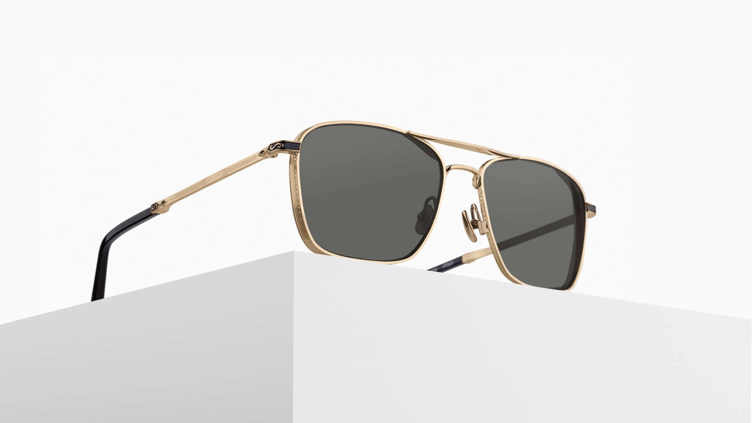 The Matsuda M3135 gold-framed aviator sunglasses with dark lenses rest on a white geometric surface against a plain, light background.