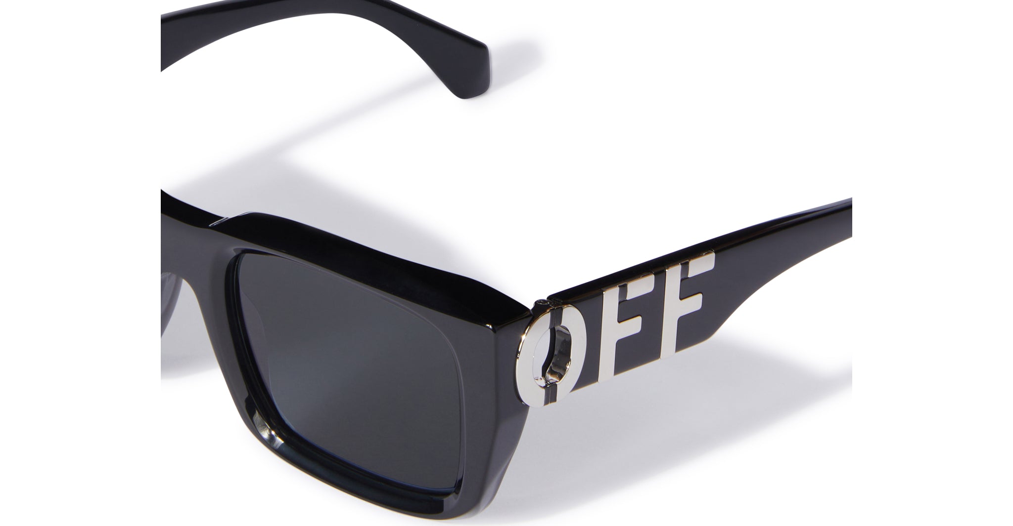 Close-up of Off-White Hays black sunglasses with dark lenses. The arm showcases large metallic cut-out letters spelling OFF, integrated into the frame design.