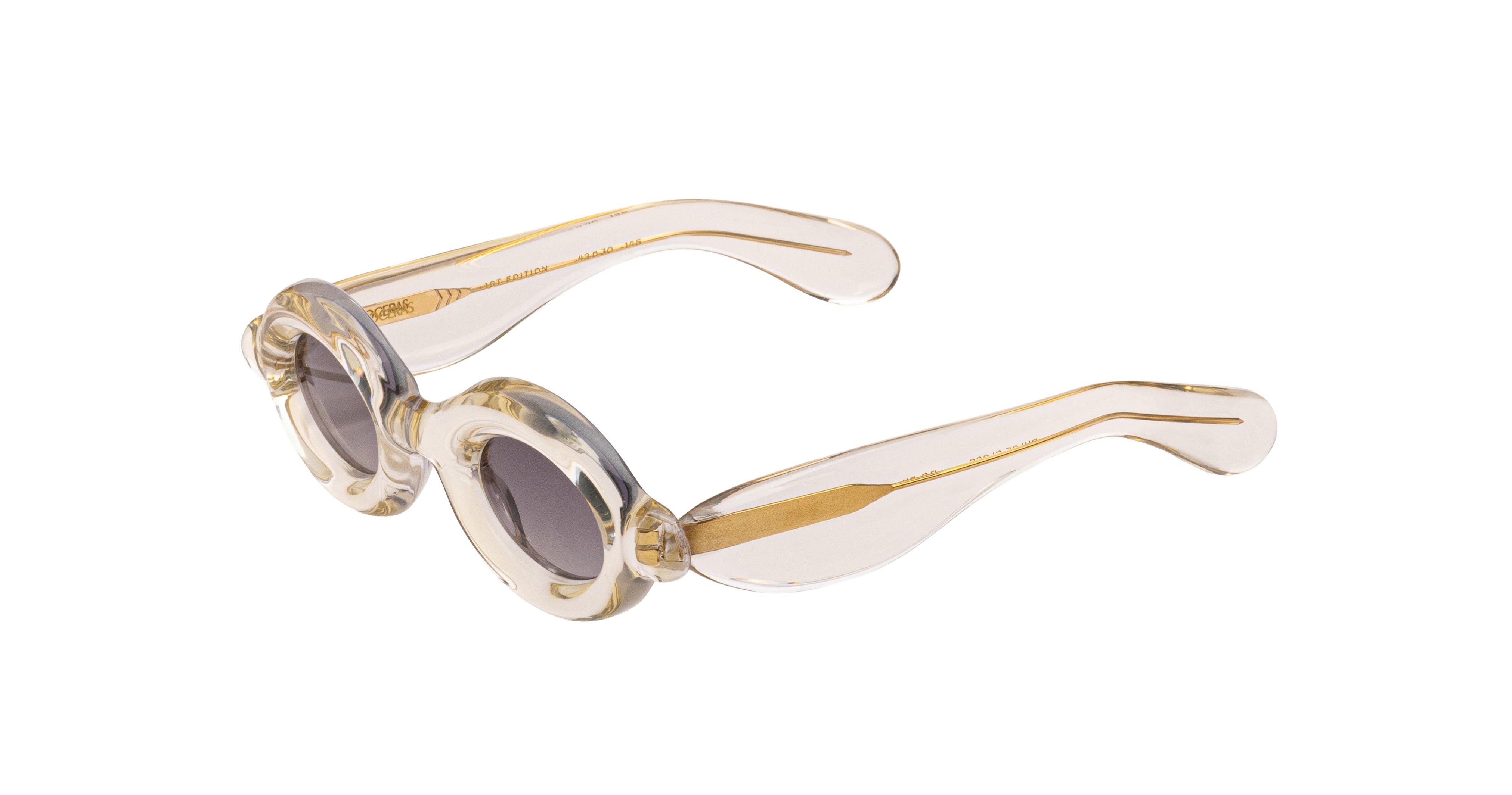 Paloceras Pebble RX Dulce Gloss sunglasses in a clear champagne frame with thick rounded oval rims, gray violet lenses, and gold-tone details, three-quarter view