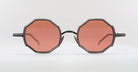A pair of round eyeglasses with octagonal frames and pink-tinted lenses, displayed against a plain white background.