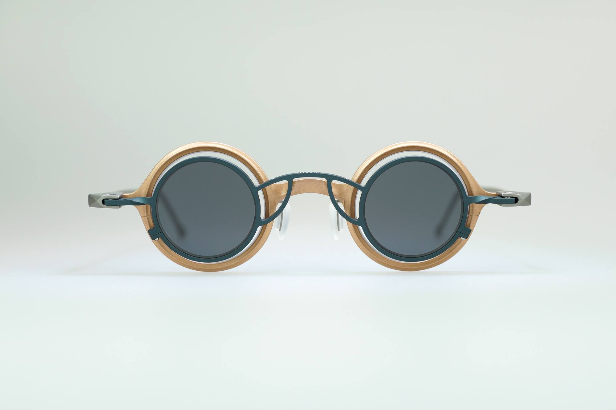 Round sunglasses with thick, light-colored wooden frames and dark lenses, featuring dark green metal accents on the bridge and arms, displayed against a plain light background.