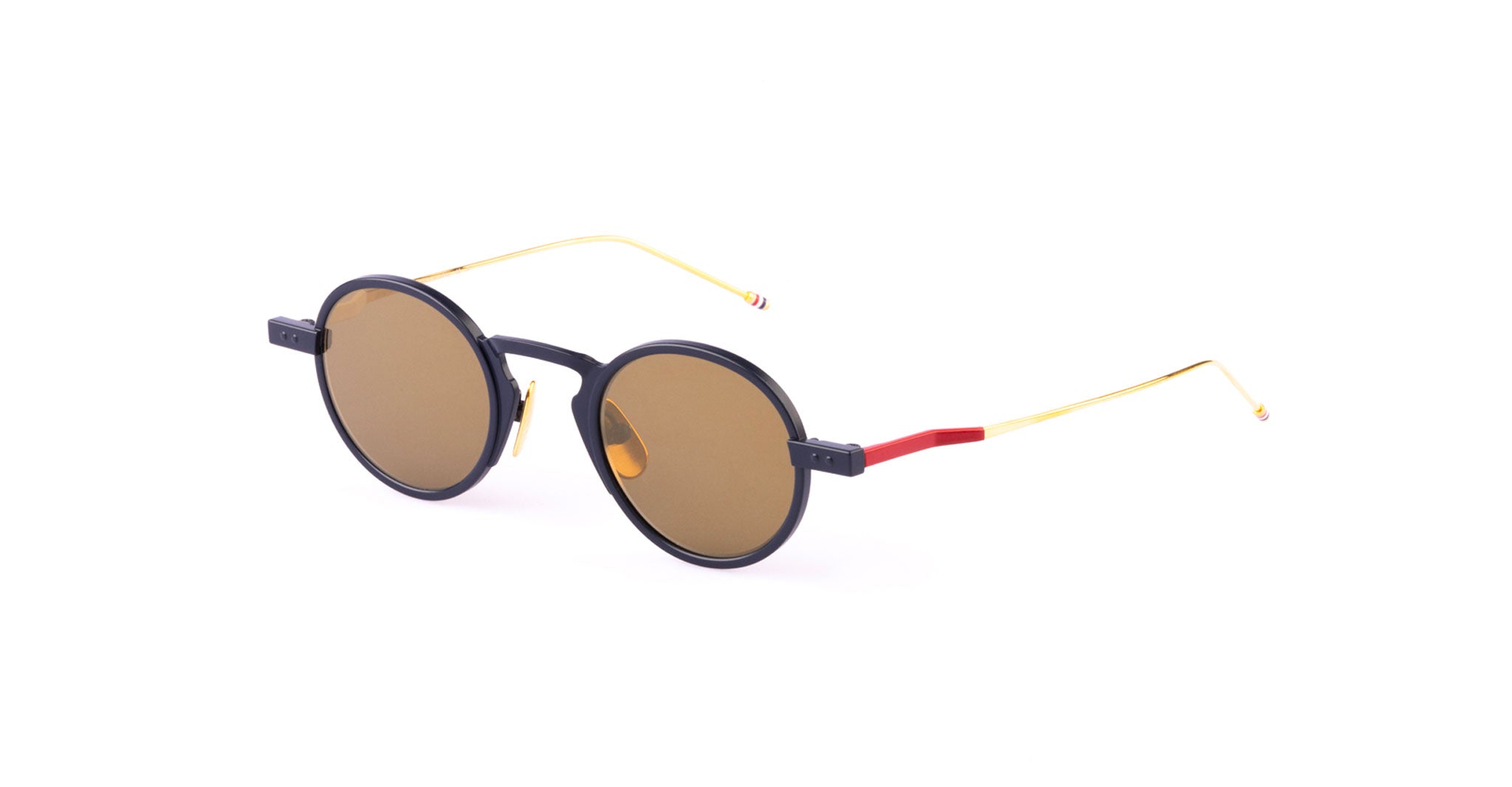 The Thom Browne 931 sunglasses feature round black frames, brown lenses, and thin gold metal arms with red accents near the hinges and red-and-white striped tips, set against a plain white background.