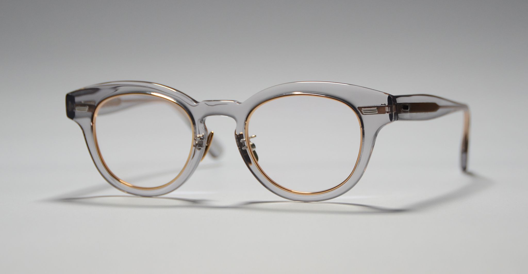 A pair of clear, round eyeglasses with gold accents around the lenses, viewed on a plain, light surface.