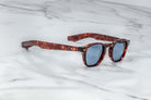 Jacques Marie Mage Zephirin limited edition acetate spectacles with blue lenses are showcased on a white marble surface—exclusive eyewear for discerning collectors.