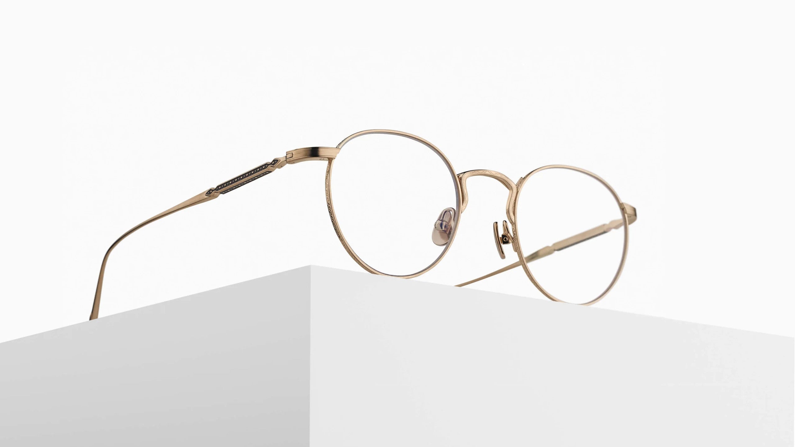 The Matsuda M3140, a pair of round gold metal eyeglasses with thin frames, is displayed on the edge of a white rectangular platform against a plain white background.