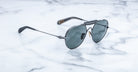 A pair of stylish aviator sunglasses with dark lenses and thin metal frames resting on a white marble surface.