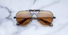 Brown-lensed aviator sunglasses with tortoiseshell arms placed on a white marble surface.