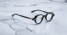 Jacques Marie Mage The Clark black round eyeglasses with gold accents, front view.