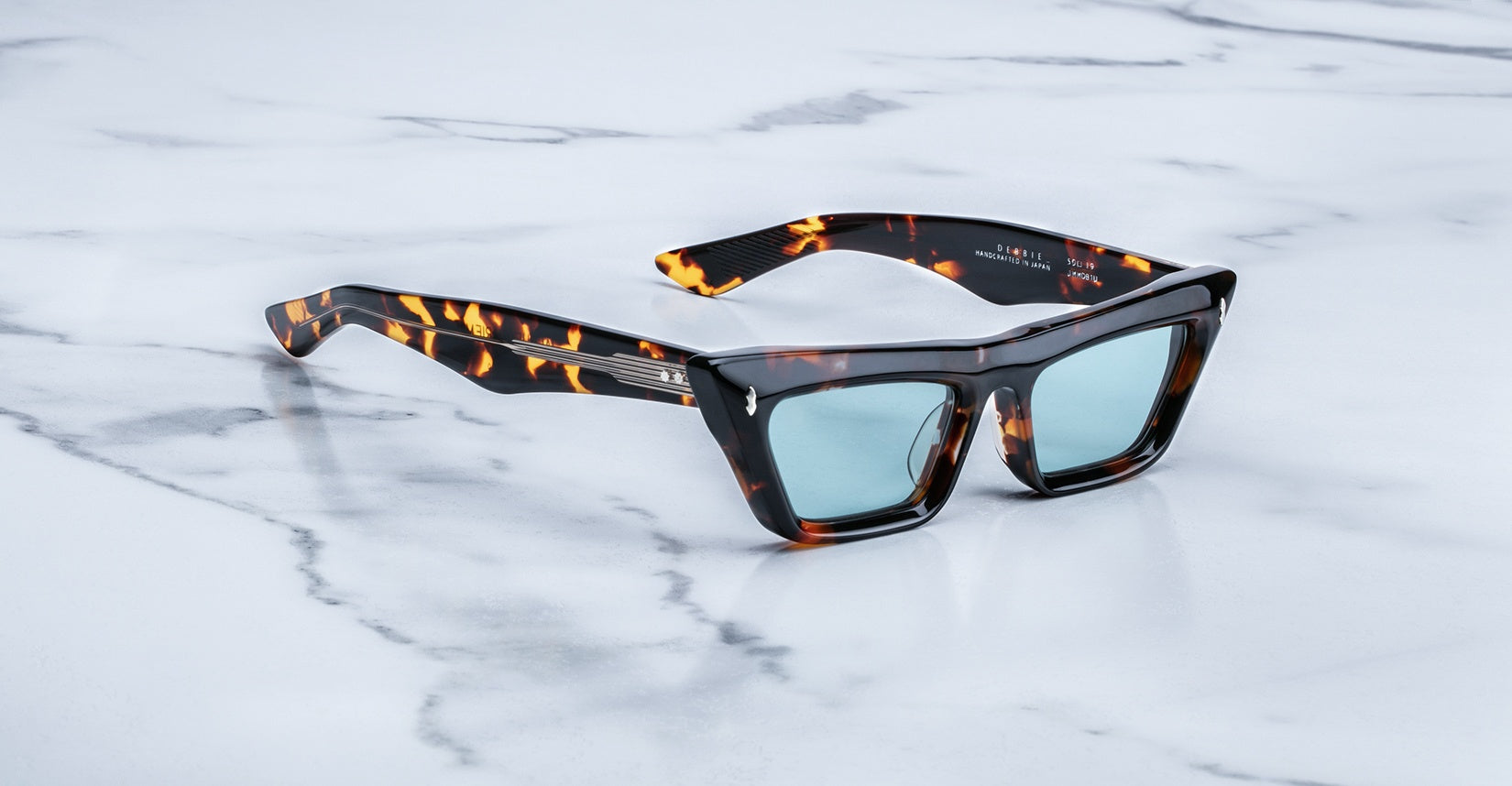 Jacques Marie Mage Debbie in Lava acetate cat-eye frame with blue-tinted lenses and tortoiseshell pattern, featuring gold arrowhead pins and exposed wirecore temples