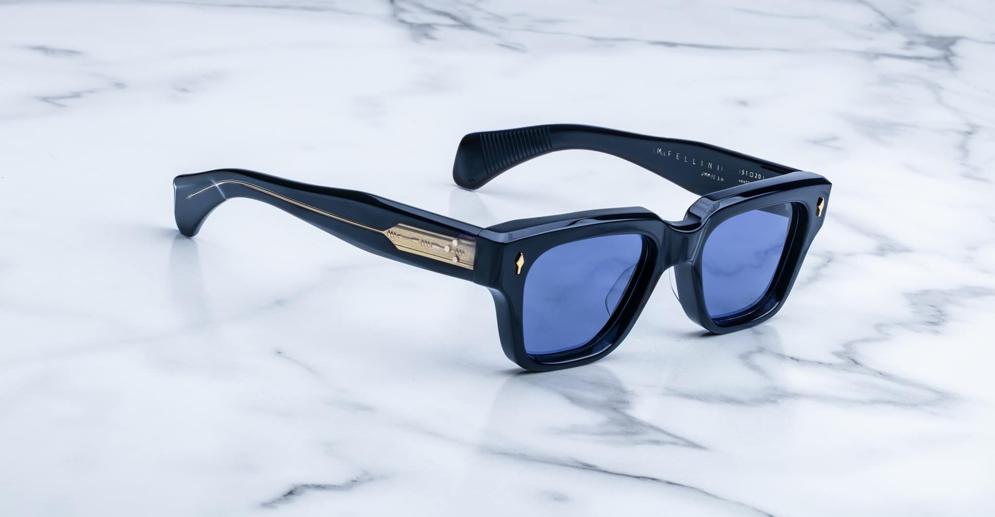 Jacques Marie Mage Fellini sunglasses with blue lenses and gold accents, shown from above.