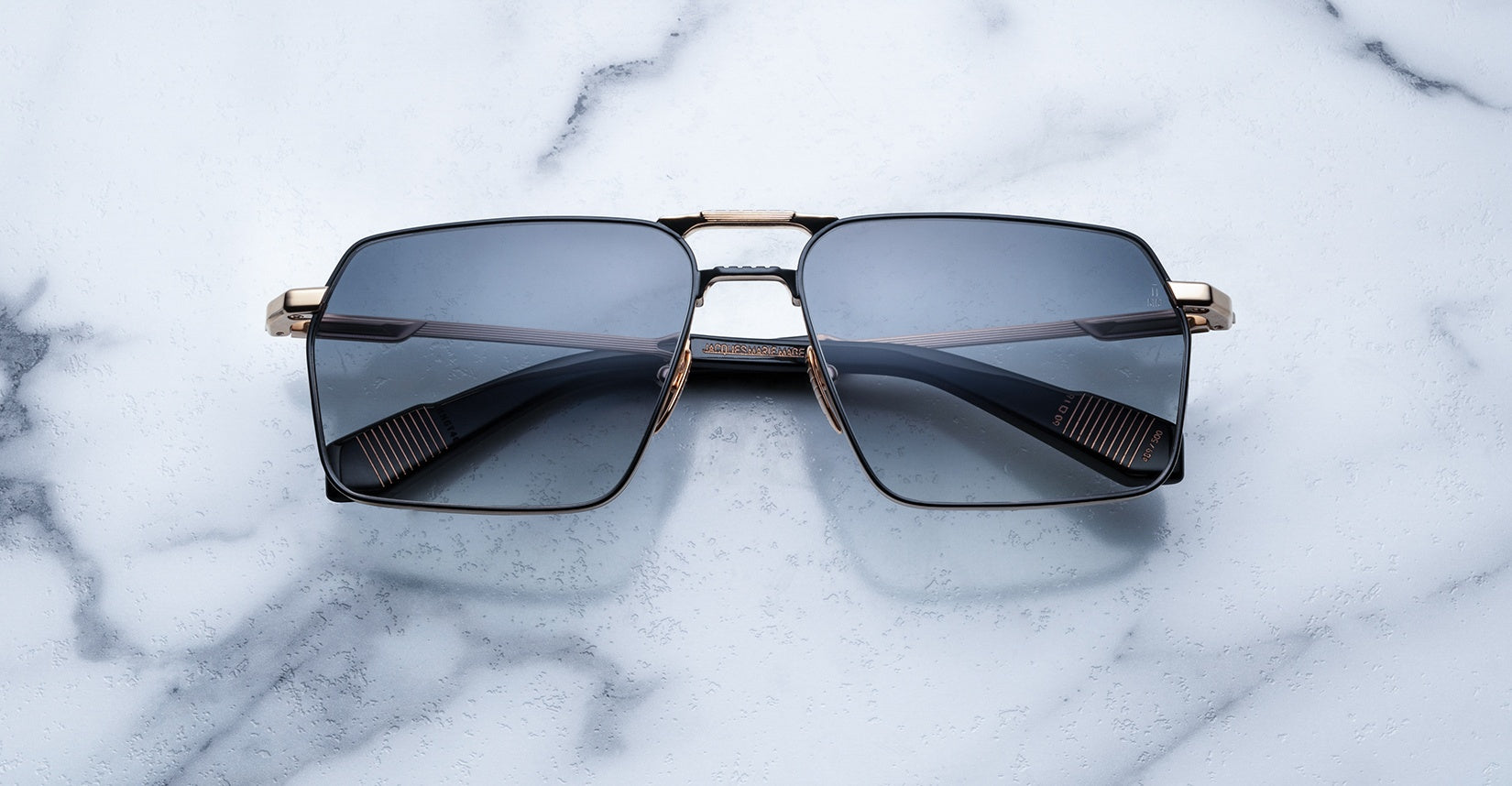 Rectangular sunglasses with dark tinted lenses and gold metal frames resting on a white marble surface.