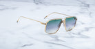 Jacques Marie Mage Jagger oversized aviator sunglasses, featuring gold frames and green gradient lenses, from Jacques Marie Mage, rest on a sleek white marble surface.