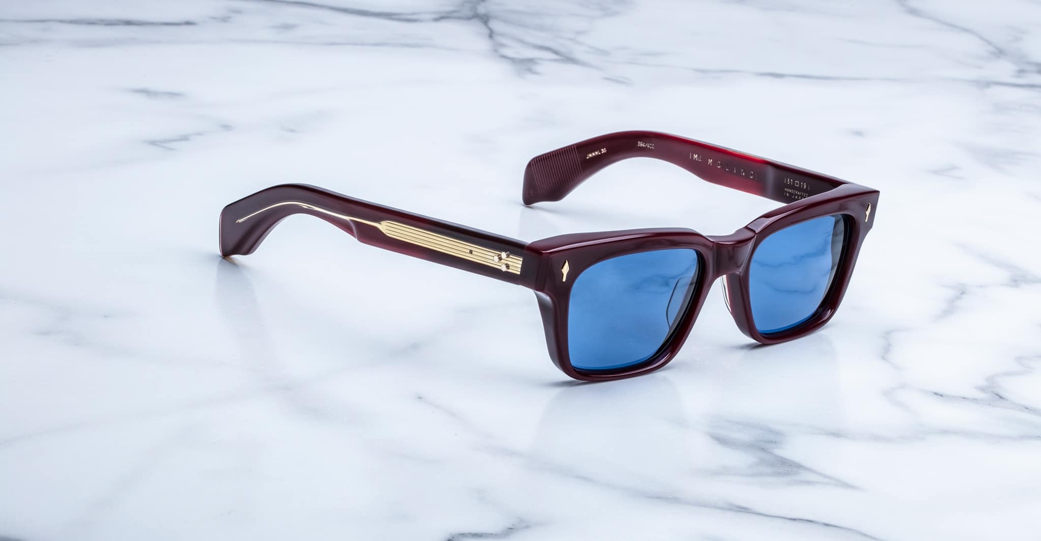 Jacques Marie Mage Molino sunglasses with blue lenses and thick maroon frames, viewed from above.