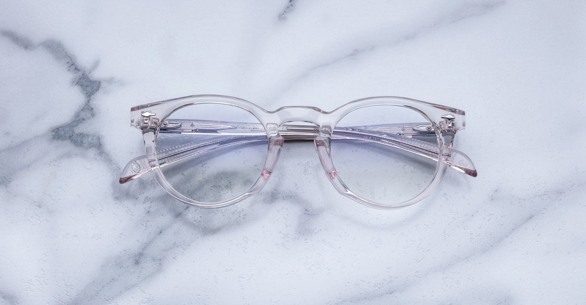 Jacques Marie Mage Percier clear round eyeglasses with pink-tinted arms, closed, viewed from above.
