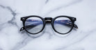 Jacques Marie Mage Percier black round eyeglasses with clear lenses, top view, eyewear displayed on white surface.