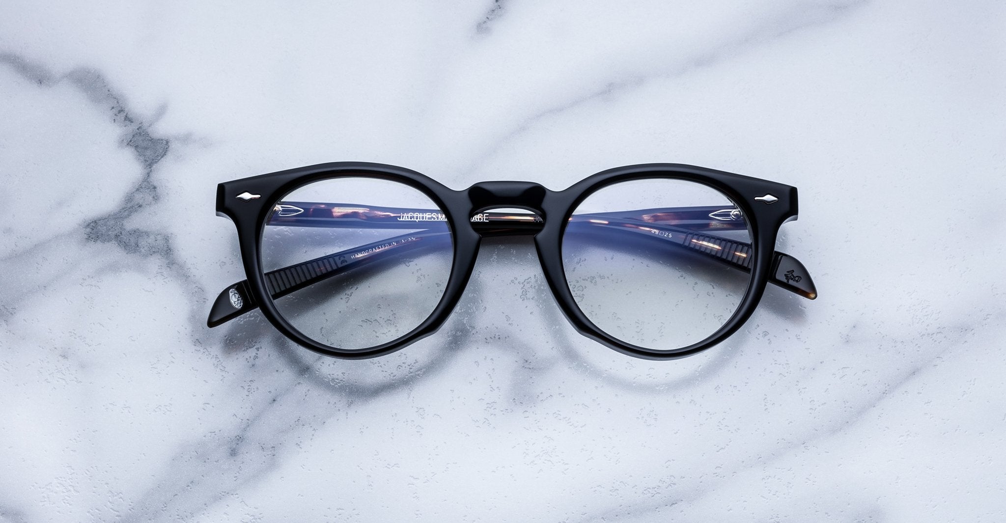 Jacques Marie Mage Percier black round eyeglasses with clear lenses, top view, eyewear displayed on white surface.