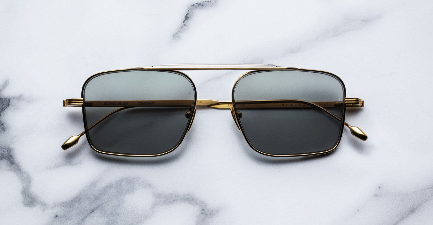 Gold-framed aviator sunglasses with dark lenses placed on a white marble surface.