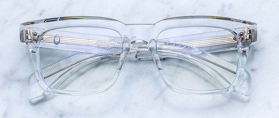 Handcrafted clear acetate Jacques Marie Mage Torino eyeglasses with bold rectangular frames and silver hinges by Jacques Marie Mage, shown on a light marble surface.