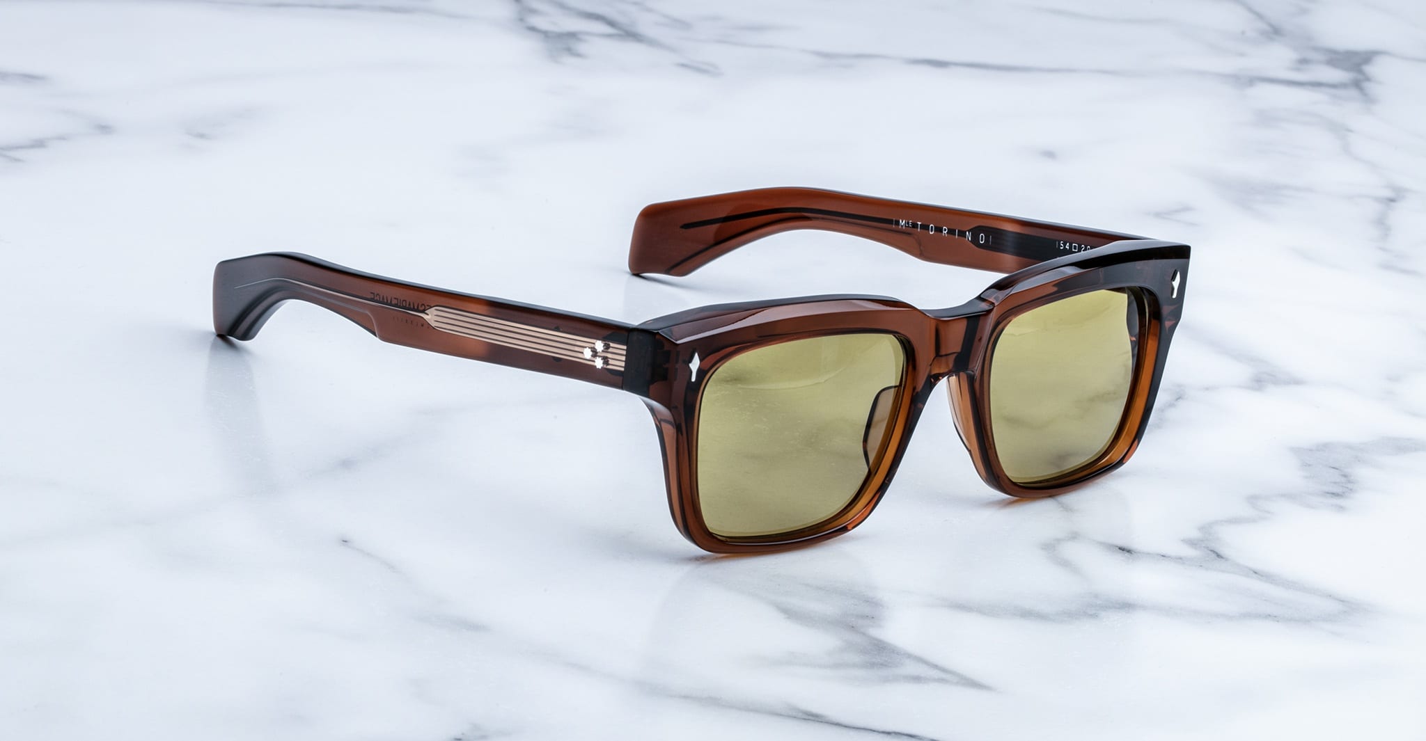 Jacques Marie Mage Torino sunglasses: brown square frames in handcrafted acetate with yellow-tinted lenses, styled on a white marble surface.
