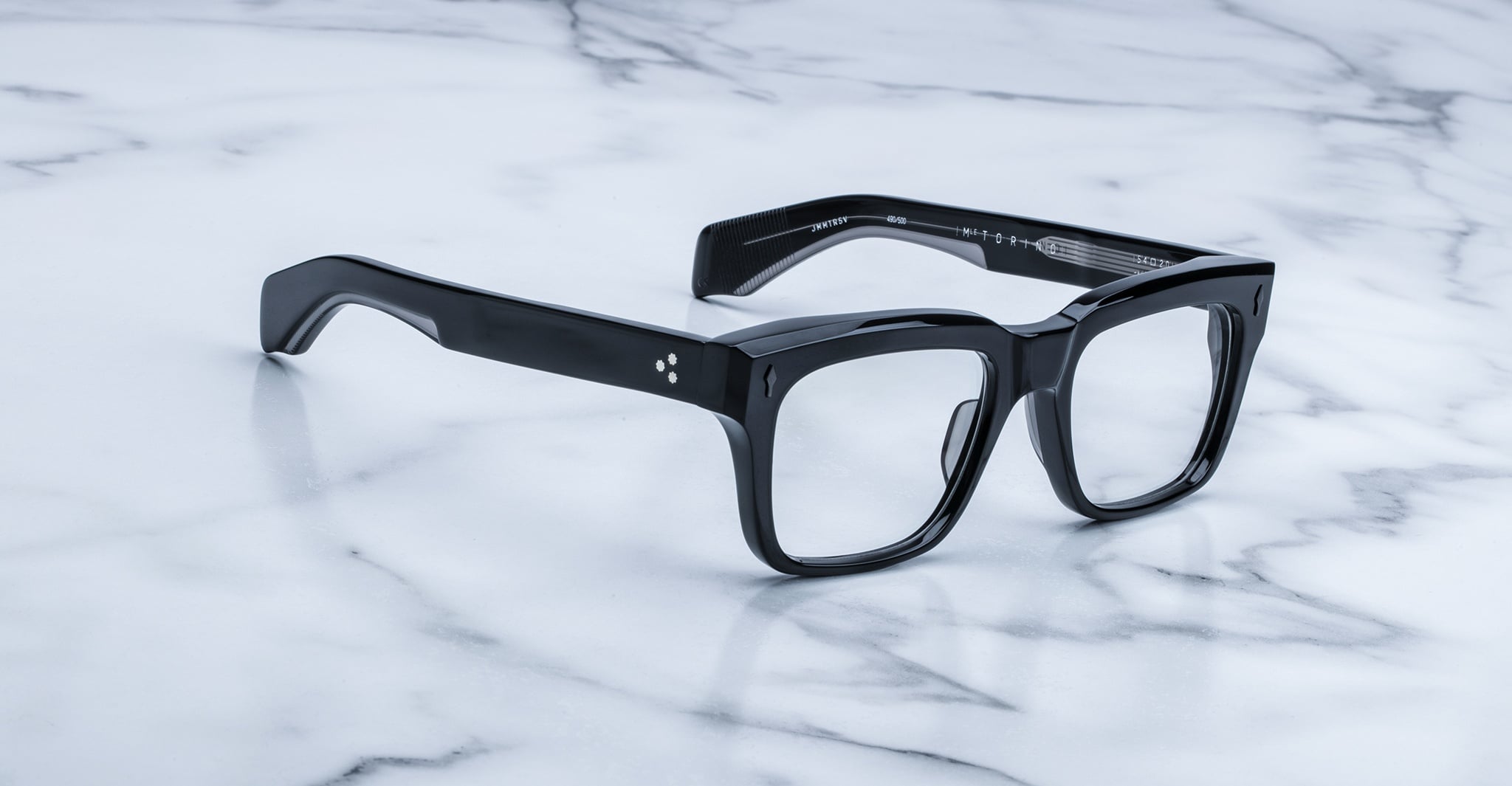 A pair of Jacques Marie Mage Torino eyeglass frames by Jacques Marie Mage sit on a white marble surface, highlighting the brand's handcrafted acetate and bold rectangular design.
