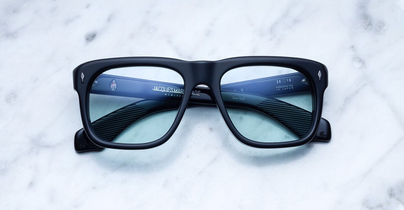 Jacques Marie Mage Yves black rectangular eyeglasses with blue-tinted lenses, shown from above.