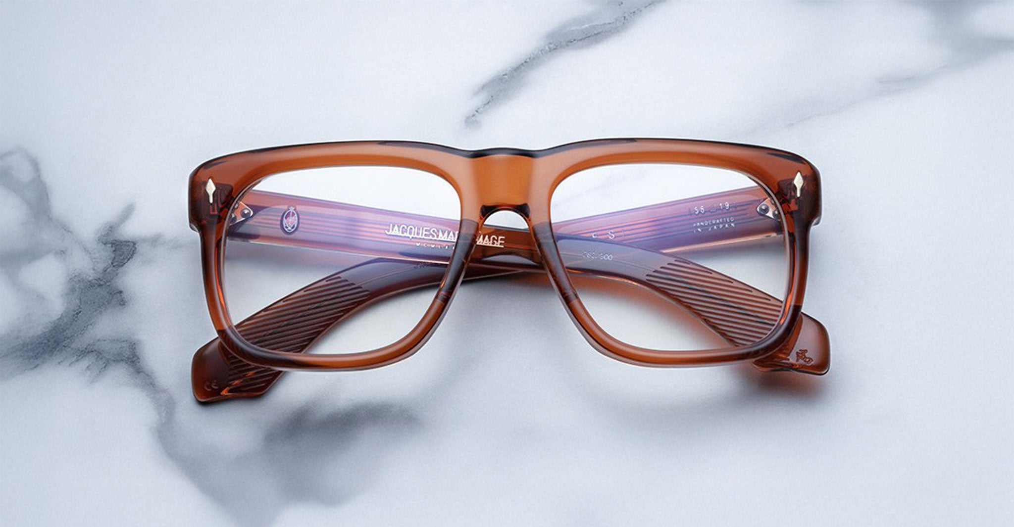Jacques Marie Mage Yves in Rootbeer optical, rectangular translucent brown acetate frame with warm amber tones, clear lenses, and signature arrowhead rivets, front view with visible engraved wirecore temples