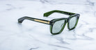 Jacques Marie Mage Yves sunglasses with green rectangular frames and gold accents, shown from the front on a white marble surface.