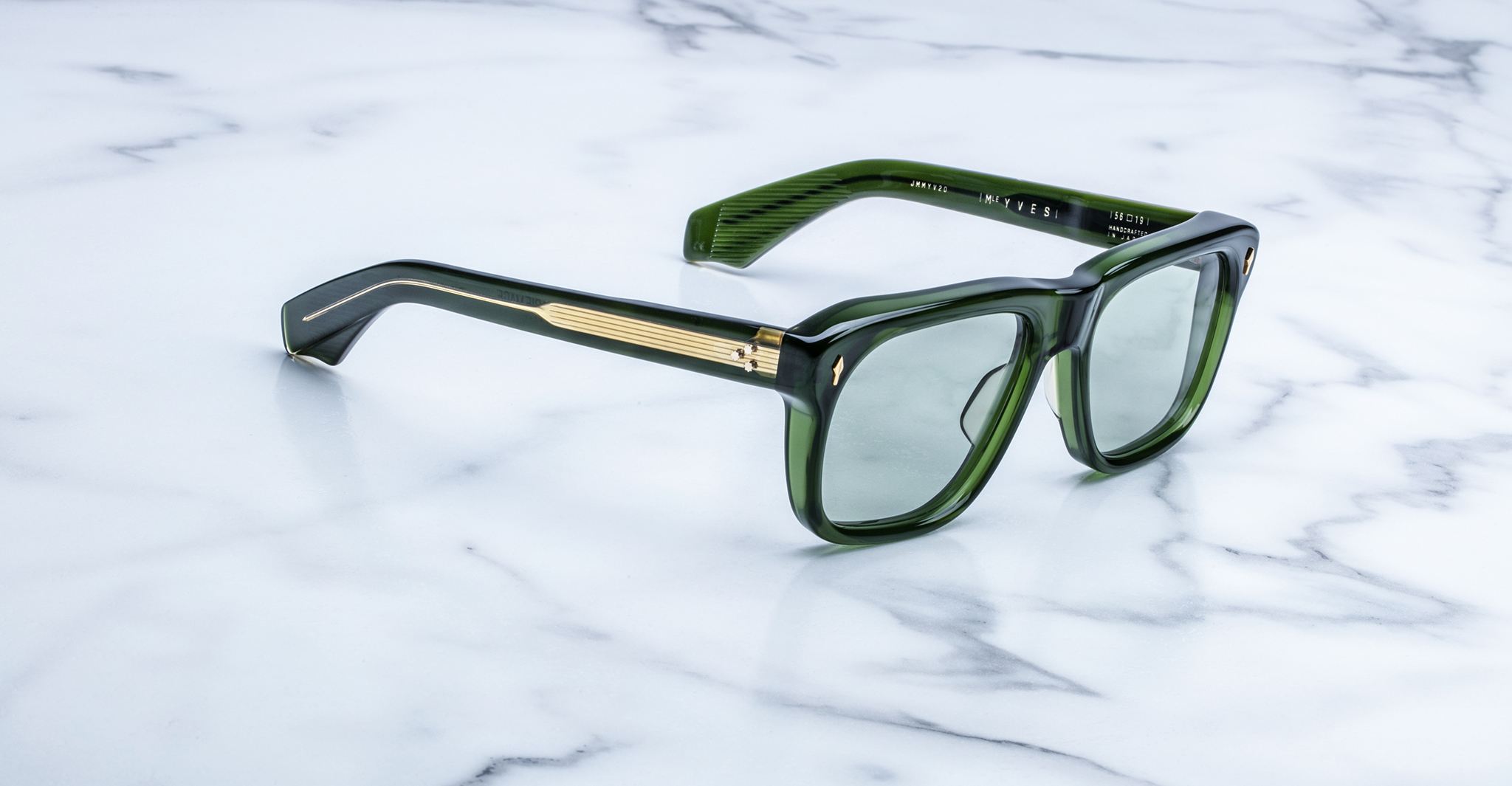 Jacques Marie Mage Yves sunglasses with green rectangular frames and gold accents, shown from the front on a white marble surface.