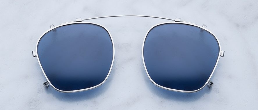 The Jacques Marie Mage Zephirin 47 Clip On features blue-tinted clip-on lenses with a silver metal frame and bridge, displayed on a light marble-textured background.