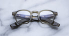A pair of Jacques Marie Mage Zephirin round dark-framed acetate eyeglasses with blue-tinted arms by Jacques Marie Mage, displayed on a light marble surface.