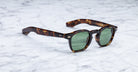 Jacques Marie Mage Zephirin tortoiseshell sunglasses with green lenses rest on white marble—a limited edition, handcrafted acetate eyewear piece by Jacques Marie Mage.