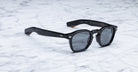 Jacques Marie Mage Zephirin black acetate sunglasses by Jacques Marie Mage rest on a white marble surface.