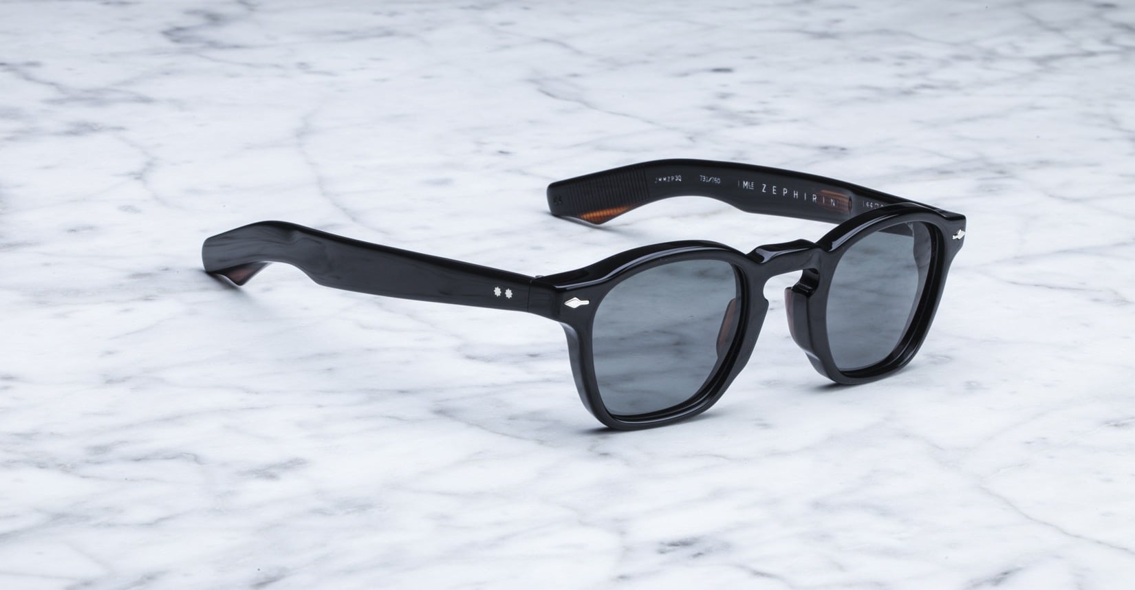 Jacques Marie Mage Zephirin black acetate sunglasses by Jacques Marie Mage rest on a white marble surface.