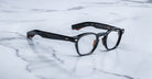 A pair of Jacques Marie Mage Zephirin eyeglasses by Jacques Marie Mage rests elegantly on a white marble surface.