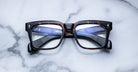 A pair of Jacques Marie Mage Torino bold rectangular eyeglass frames in tortoiseshell handcrafted acetate by Jacques Marie Mage rests on a white marble surface.