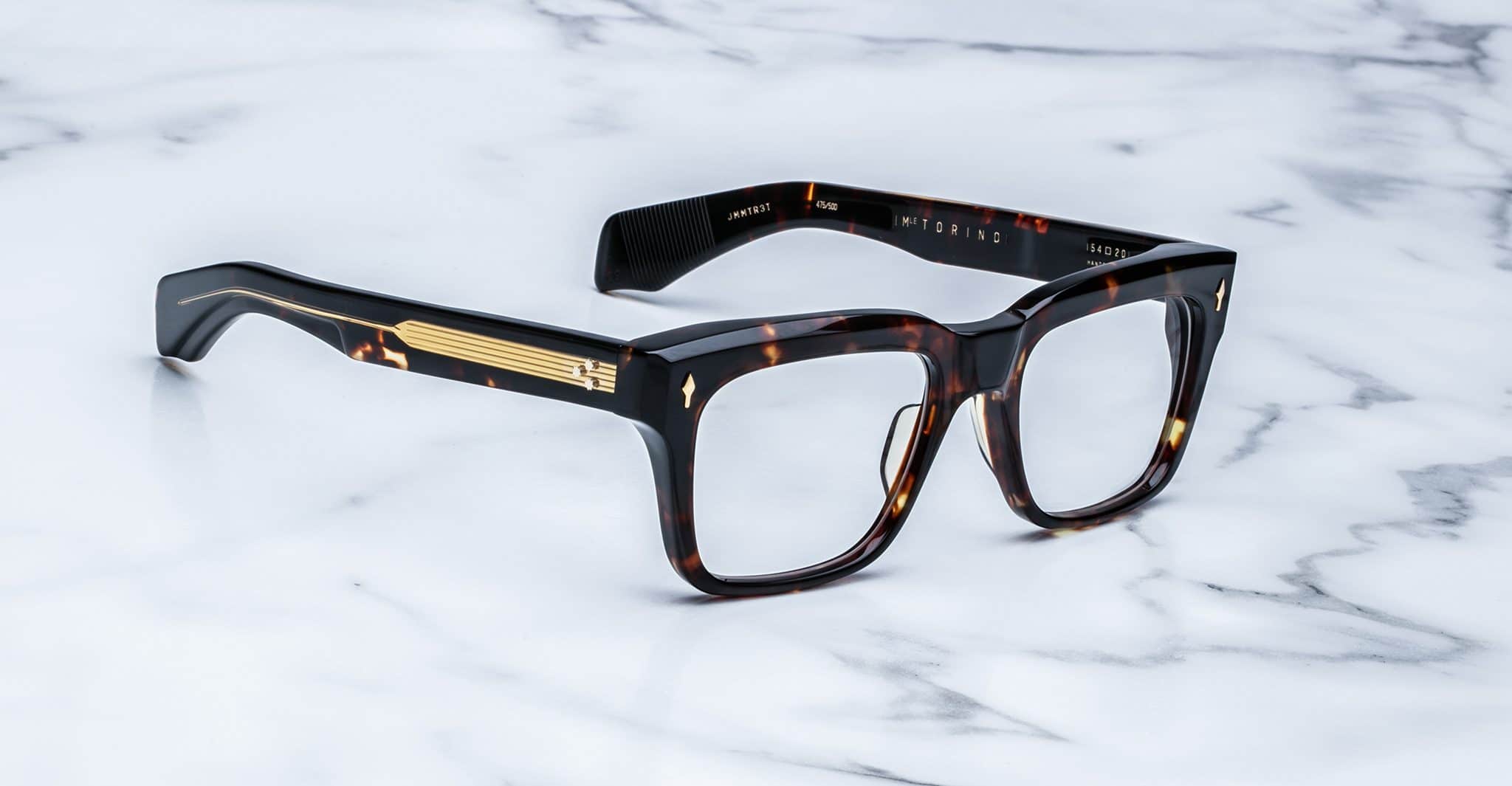 Jacques Marie Mage Torino eyeglasses: bold, handcrafted acetate frames in tortoiseshell with gold temple detailing, inspired by the iconic Jacques Marie Mage brand, elegantly displayed on a white marble surface.