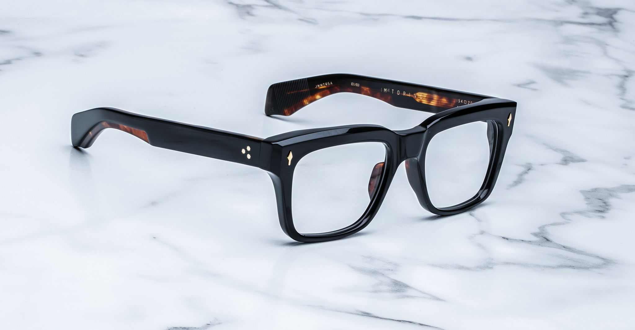 The Jacques Marie Mage Torino features bold rectangular acetate frames with thick black rims and subtle amber details, handcrafted by Jacques Marie Mage, displayed on a white marble surface.